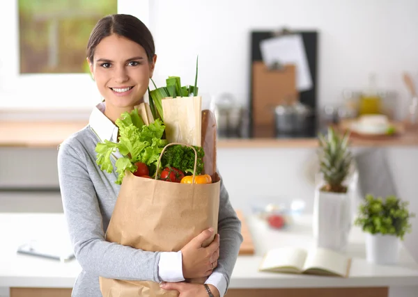 Giovane donna che tiene la spesa con verdure In piedi in cucina. — Foto Stock