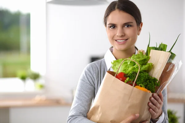 Giovane donna che tiene la spesa con verdure In piedi in cucina. — Foto Stock