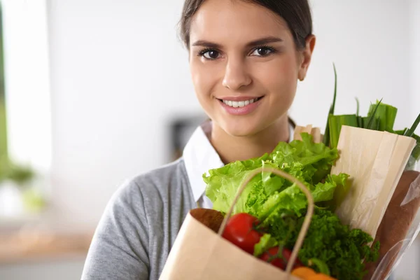 Mladá žena držící nákupní tašku se zeleninou Stojící v kuchyni. — Stock fotografie