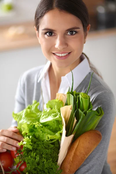 야채 가방을 들고 부엌에 서 있는 젊은 여자. — 스톡 사진
