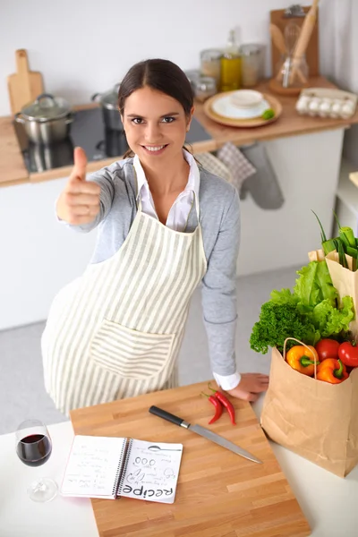 Mujer en delantal de pie sobre el escritorio con bolsa de comestibles mostrando ok — Foto de Stock