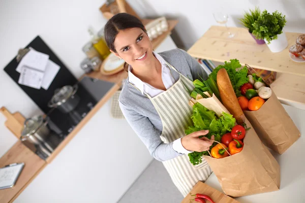 Donna con le borse della spesa in cucina a casa, in piedi vicino alla scrivania — Foto Stock