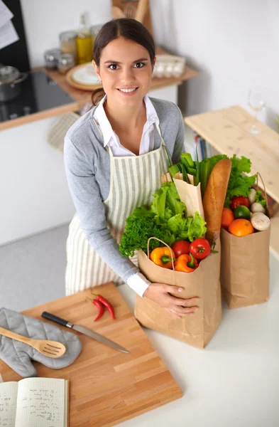 Mujer con bolsas de compras en la cocina en casa, de pie cerca del escritorio — Foto de Stock
