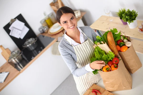 Donna con le borse della spesa in cucina a casa, in piedi vicino alla scrivania — Foto Stock