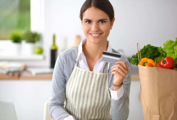 Mujer sonriente compras en línea utilizando la computadora y la tarjeta de crédito en la cocina — Foto de Stock