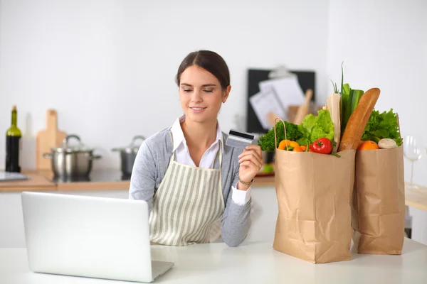 Uśmiechnięta kobieta zakupy online przy użyciu komputera i karty kredytowej w kuchni — Zdjęcie stockowe