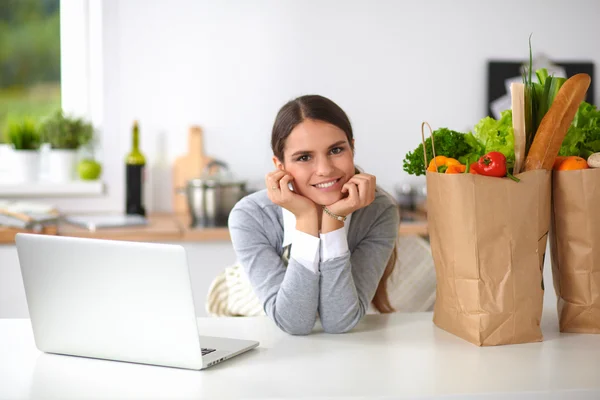Beautiful young woman cooking looking at laptop screen with receipt in the kitchen — Stock Photo, Image