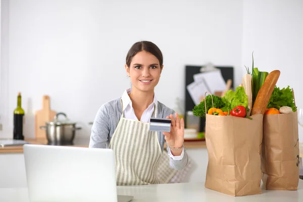 Smiling woman online shopping using computer and credit card in kitchen — Stock Photo, Image