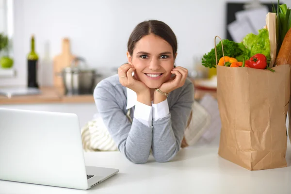 Beautiful young woman cooking looking at laptop screen with receipt in the kitchen — Stock Photo, Image