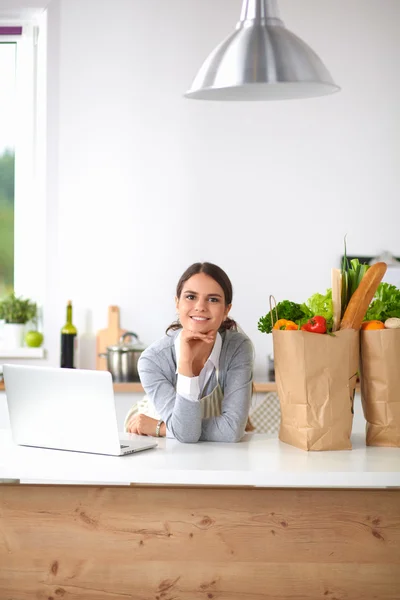 Schöne junge Frau kocht mit Blick auf Laptop-Bildschirm mit Quittung in der Küche — Stockfoto