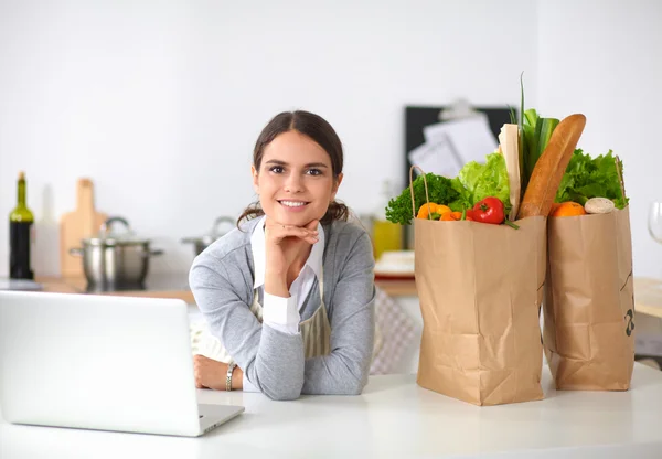 Beautiful young woman cooking looking at laptop screen with receipt in the kitchen — Stock Photo, Image