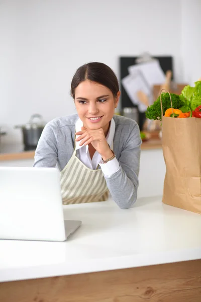 Hermosa joven cocina mirando a la pantalla del ordenador portátil con recibo en la cocina —  Fotos de Stock