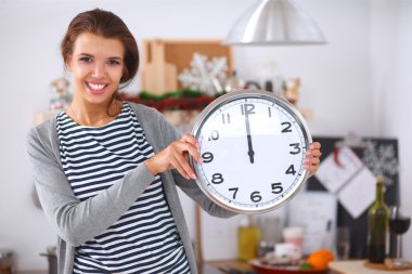 Mutlu genç kadın Noel süslemeli mutfakta saat gösteriyor.