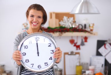 Mutlu genç kadın Noel süslemeli mutfakta saat gösteriyor.