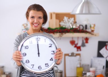 Mutlu genç kadın Noel süslemeli mutfakta saat gösteriyor.