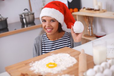 Mutlu genç bayan gülümsüyor Noel hazırlıklarıyla eğleniyor Noel Baba şapkası takıyor.