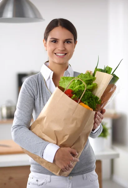 Jonge vrouw met boodschappentas met groenten Staande in de keuken. — Stockfoto