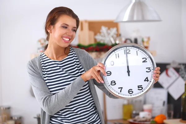 Happy young woman showing clock in christmas decorated kitchen