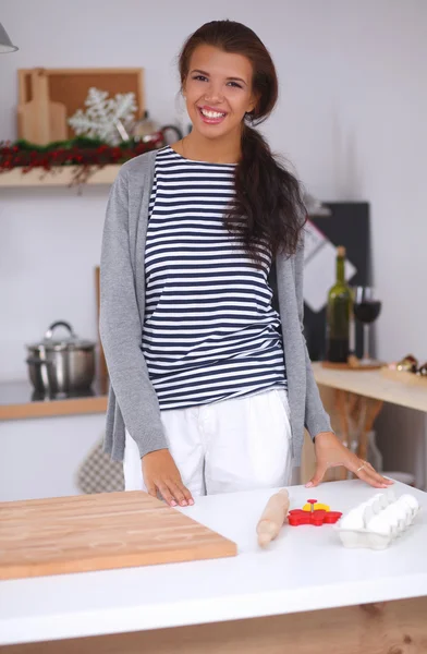 Glimlachende jonge vrouw in de keuken, geïsoleerd op kerst achtergrond — Stockfoto