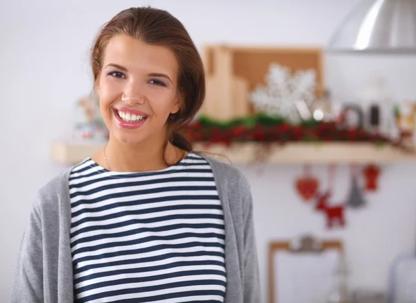 Glimlachende jonge vrouw in de keuken, geïsoleerd op kerst achtergrond — Stockfoto