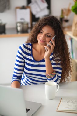 telefonda konuşuyor ve mutfaktaki dizüstü bilgisayar üzerinde çalışan genç güzel kadın portresi