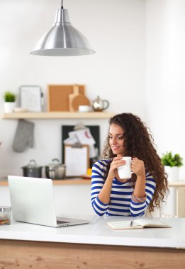 kahve fincanı ve dizüstü evde mutfakta gülümseyen genç kadın