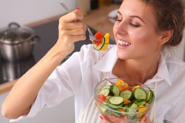 Genç kadın modern mutfakta taze salata yiyor.