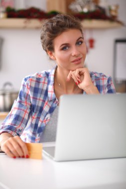 Mutfakta bilgisayar ve kredi kartı kullanan gülümseyen bir kadın.