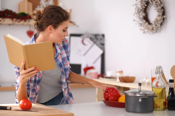 Jovem mulher lendo livro de receitas na cozinha, à procura de receita — Fotografia de Stock