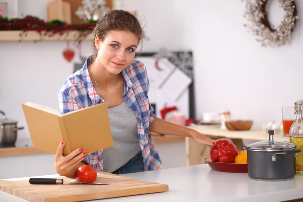 Ung kvinna läser kokbok i köket, letar efter recept — Stockfoto