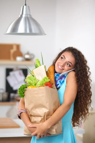 Ung kvinna som håller i matkassen med grönsaker Står i köket. — Stockfoto