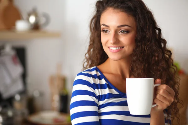 Portrait of young woman with cup against kitchen interior background. — Stock Photo, Image