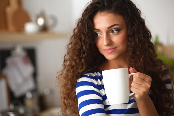 Porträt einer jungen Frau mit Tasse vor Kücheninterieur. — Stockfoto