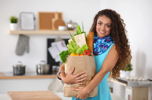 Giovane donna che tiene la spesa con verdure In piedi in cucina. — Foto Stock