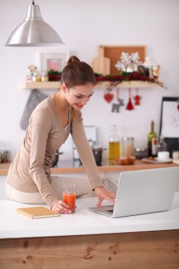 mutfağında suyu yudumlarken bir dizüstü bilgisayar kullanan kadın