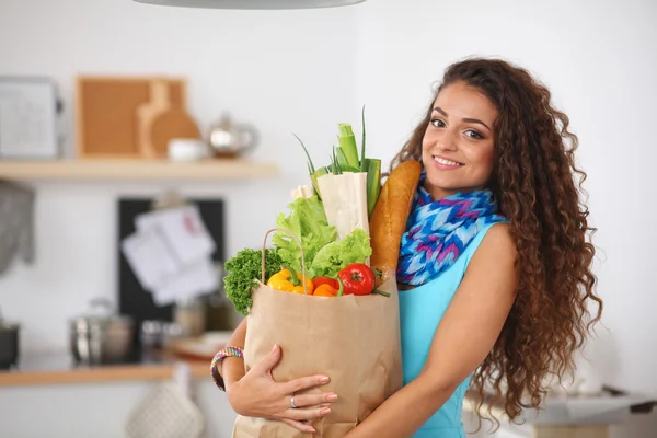 Junge Frau hält Einkaufstüte mit Gemüse in der Küche. — Stockfoto