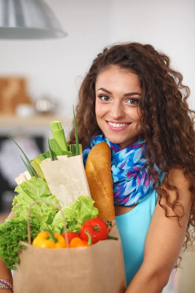 Giovane donna che tiene la spesa con verdure In piedi in cucina. — Foto Stock