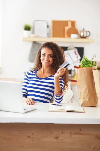 Lachende vrouw online winkelen met behulp van computer en creditcard in de keuken — Stockfoto