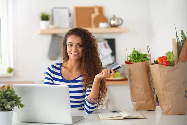 Lachende vrouw online winkelen met behulp van computer en creditcard in de keuken — Stockfoto