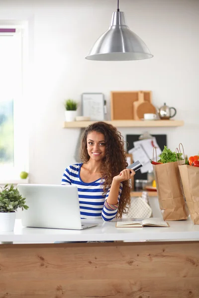 Smiling woman online shopping using computer and credit card in kitchen — Stock Photo, Image