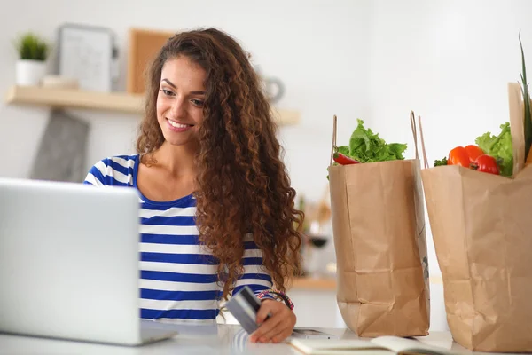 Smiling woman online shopping using computer and credit card in kitchen — Stock Photo, Image