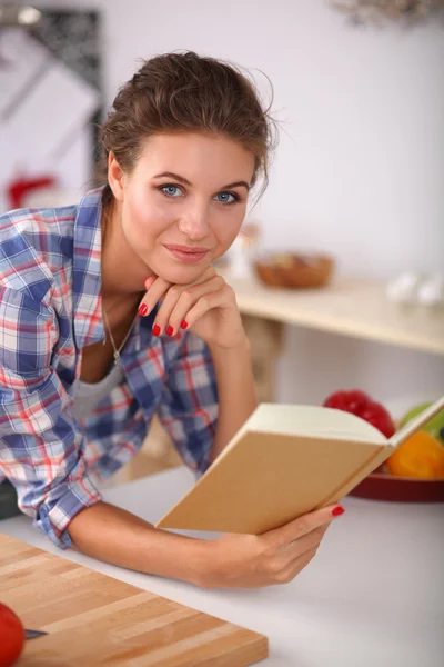 Jovem mulher lendo livro de receitas na cozinha, à procura de receita — Fotografia de Stock