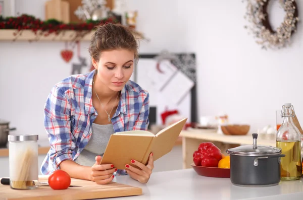 Jovem mulher lendo livro de receitas na cozinha, à procura de receita — Fotografia de Stock