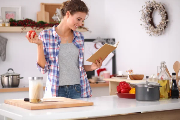 Young woman reading cookbook in the kitchen, looking for recipe — Stock Photo, Image