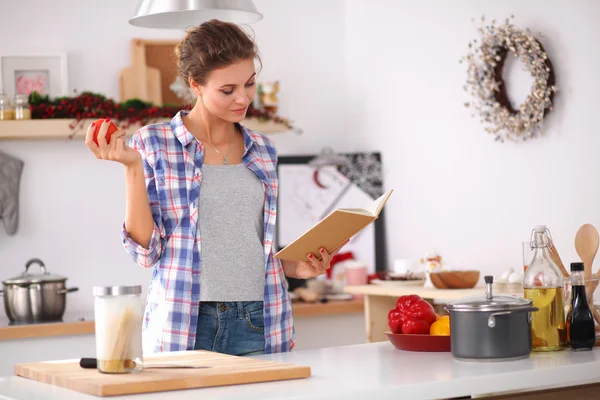 Mutfakta yemek kitabı okuyan genç bir kadın yemek tarifi arıyor. — Stok fotoğraf