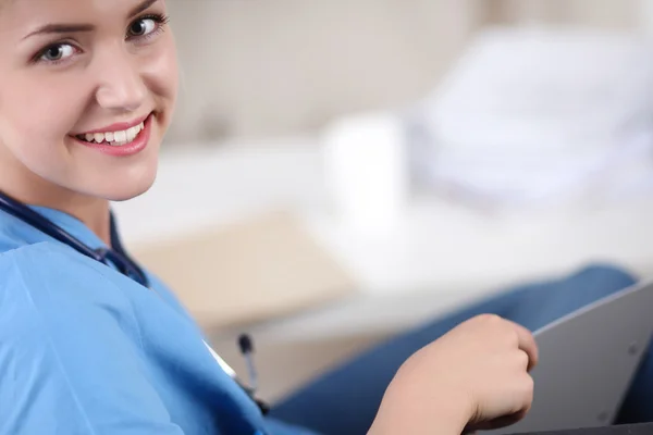 Portrait of a happy young doctor sitting on the sofa with folde — Stock Photo, Image