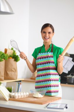 Mutfakta gülümseyen genç bir kadın, arka planda soyutlanmış.