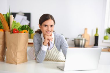 Güzel genç bayan yemek pişiriyor. Mutfakta makbuzu olan dizüstü bilgisayara bakıyor.