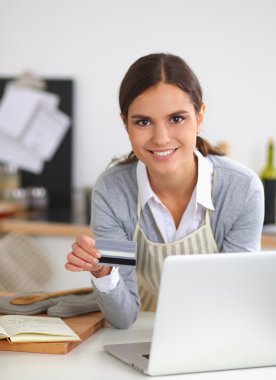 Mutfakta bilgisayar ve kredi kartı kullanan gülümseyen bir kadın.