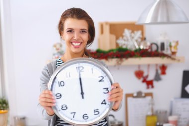 Mutlu genç kadın Noel süslemeli mutfakta saat gösteriyor.